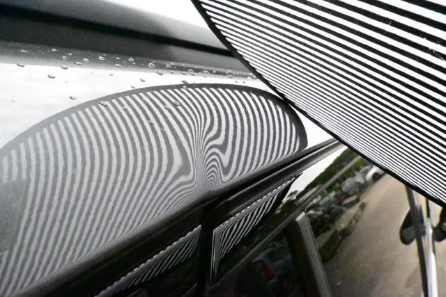 Schadendokumentation mit Streifensegel: Das gespiegelte Streifenmuster macht kleinste Verformungen im Lack einer dunklen Fahrzeugflanke sichtbar.
